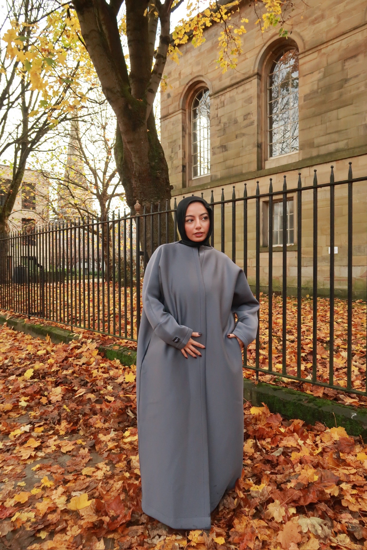 one model wearing neoprene scuba abayas in gray and maroon colors, standing outdoors with autumn leaves on the ground.