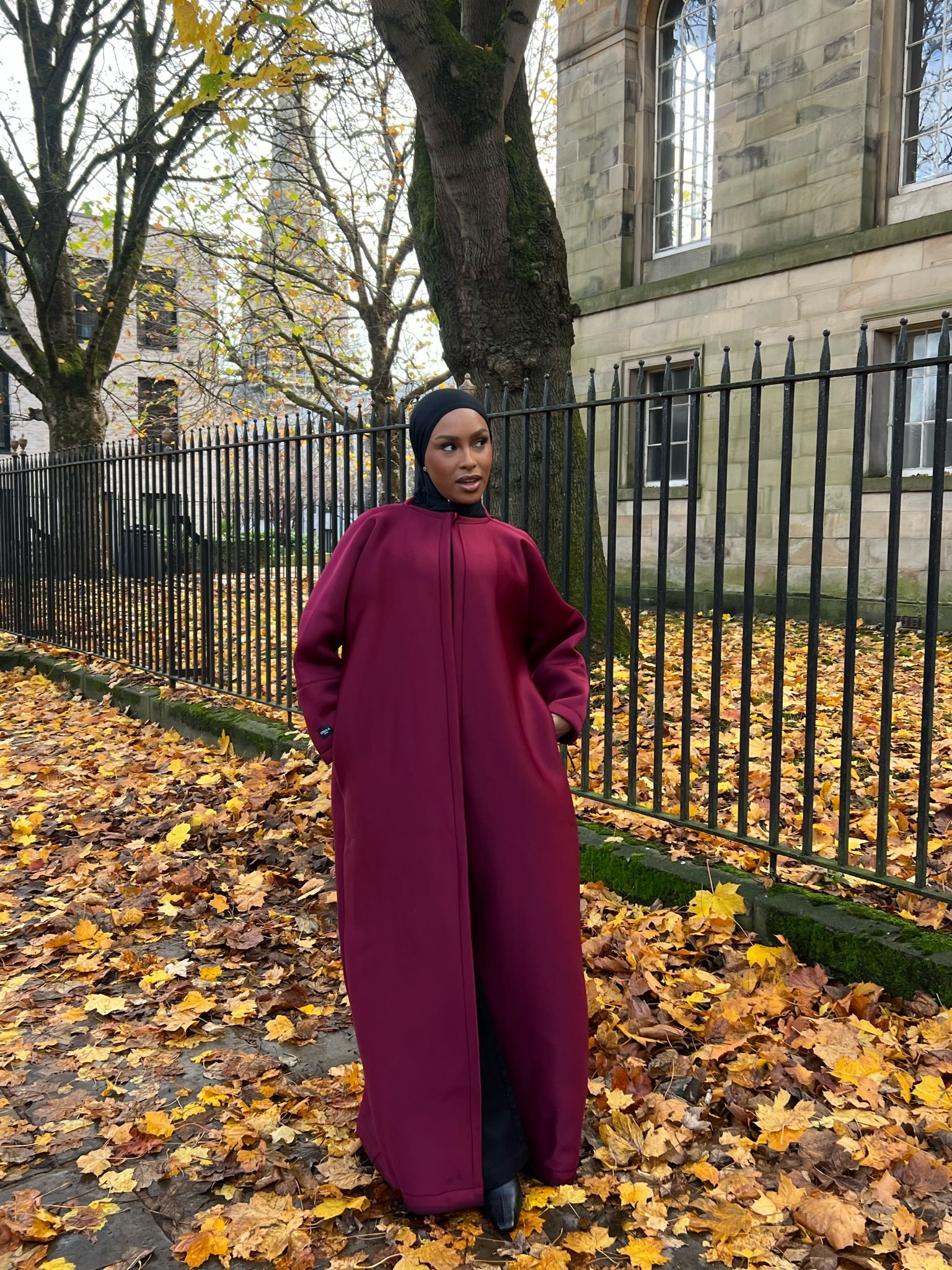 Two models wearing neoprene scuba abayas in gray and maroon colors, standing outdoors with autumn leaves on the ground.