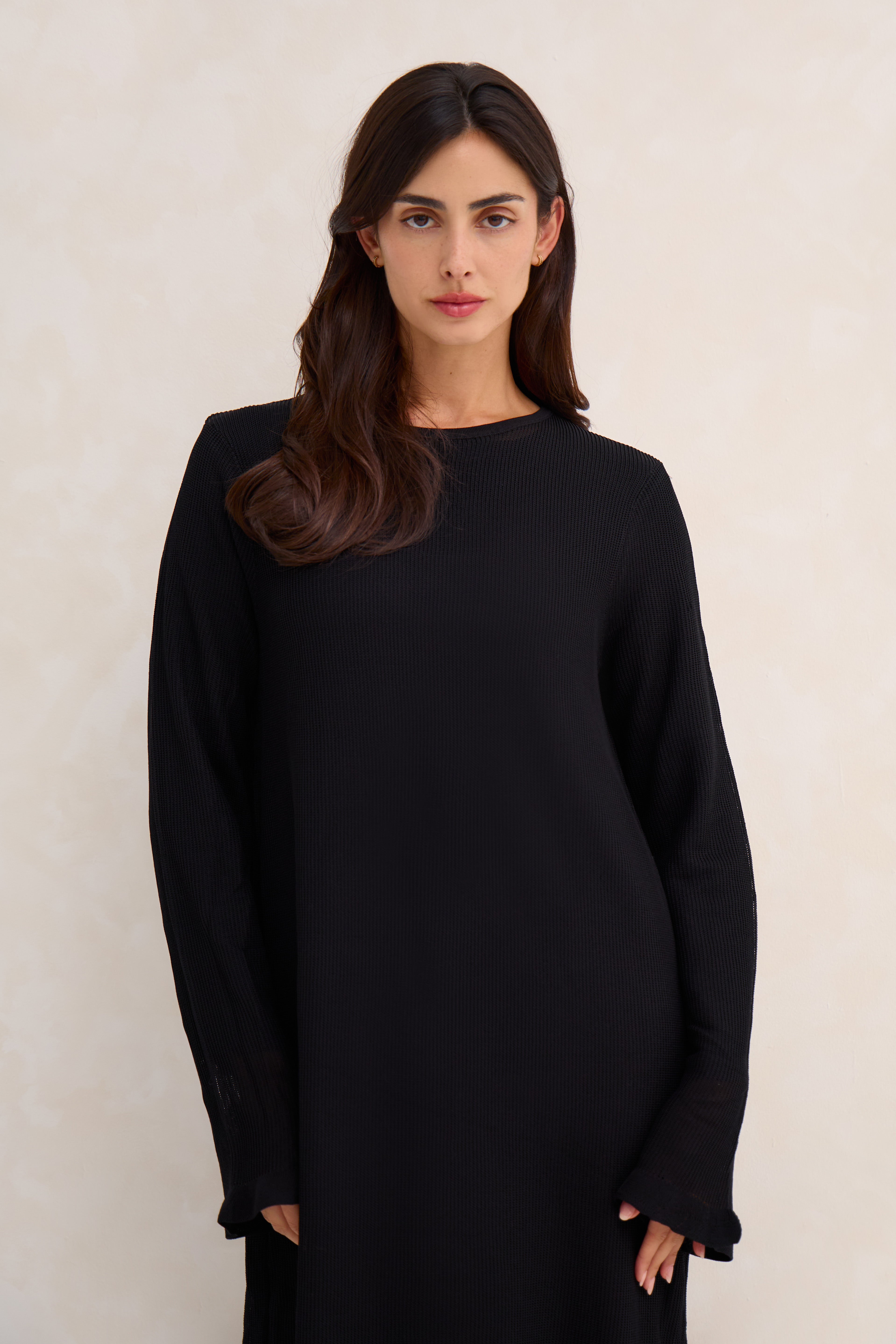 Woman wearing a black crochet abaya against a plain background
