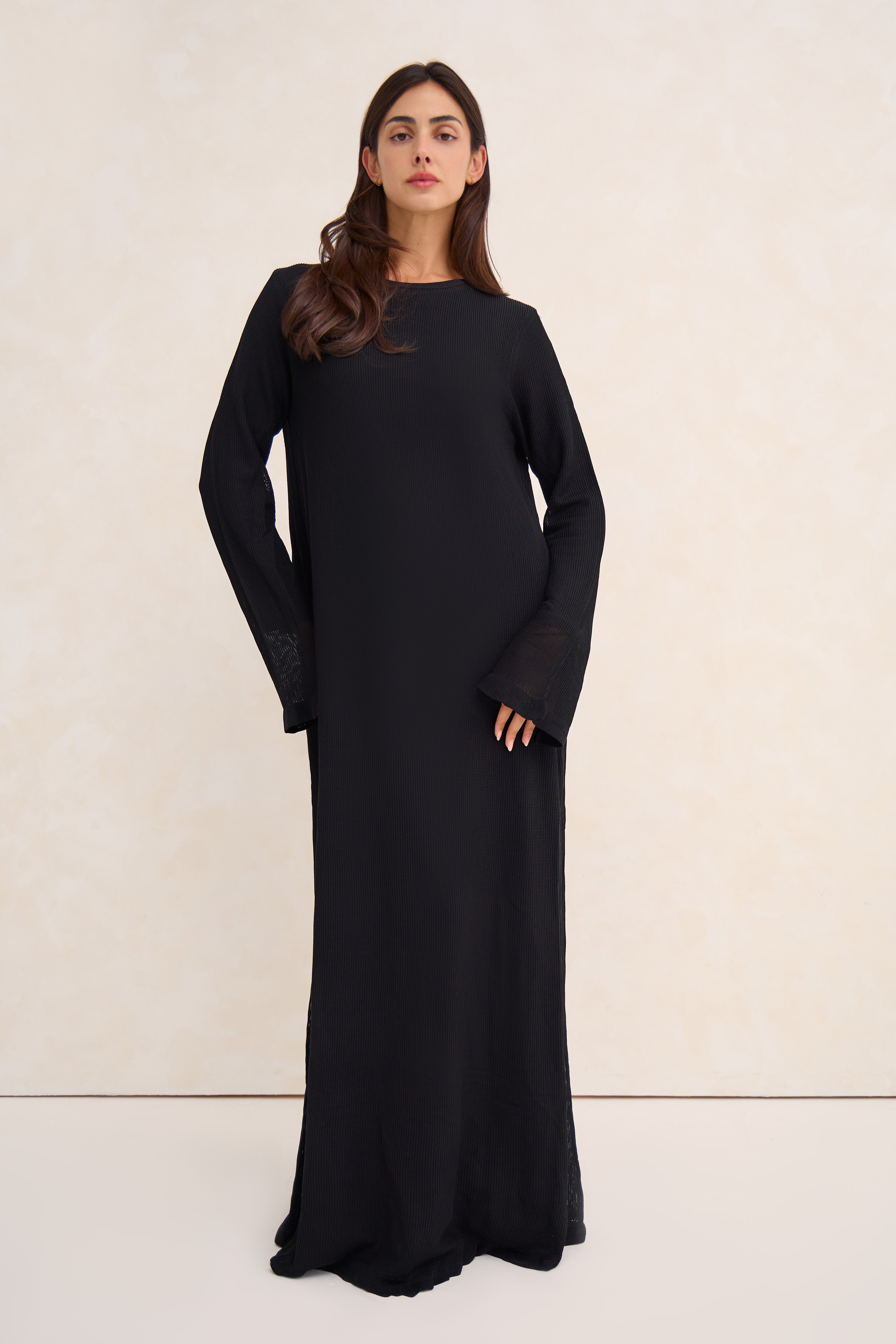 Woman wearing a long black crochet abaya against a white background