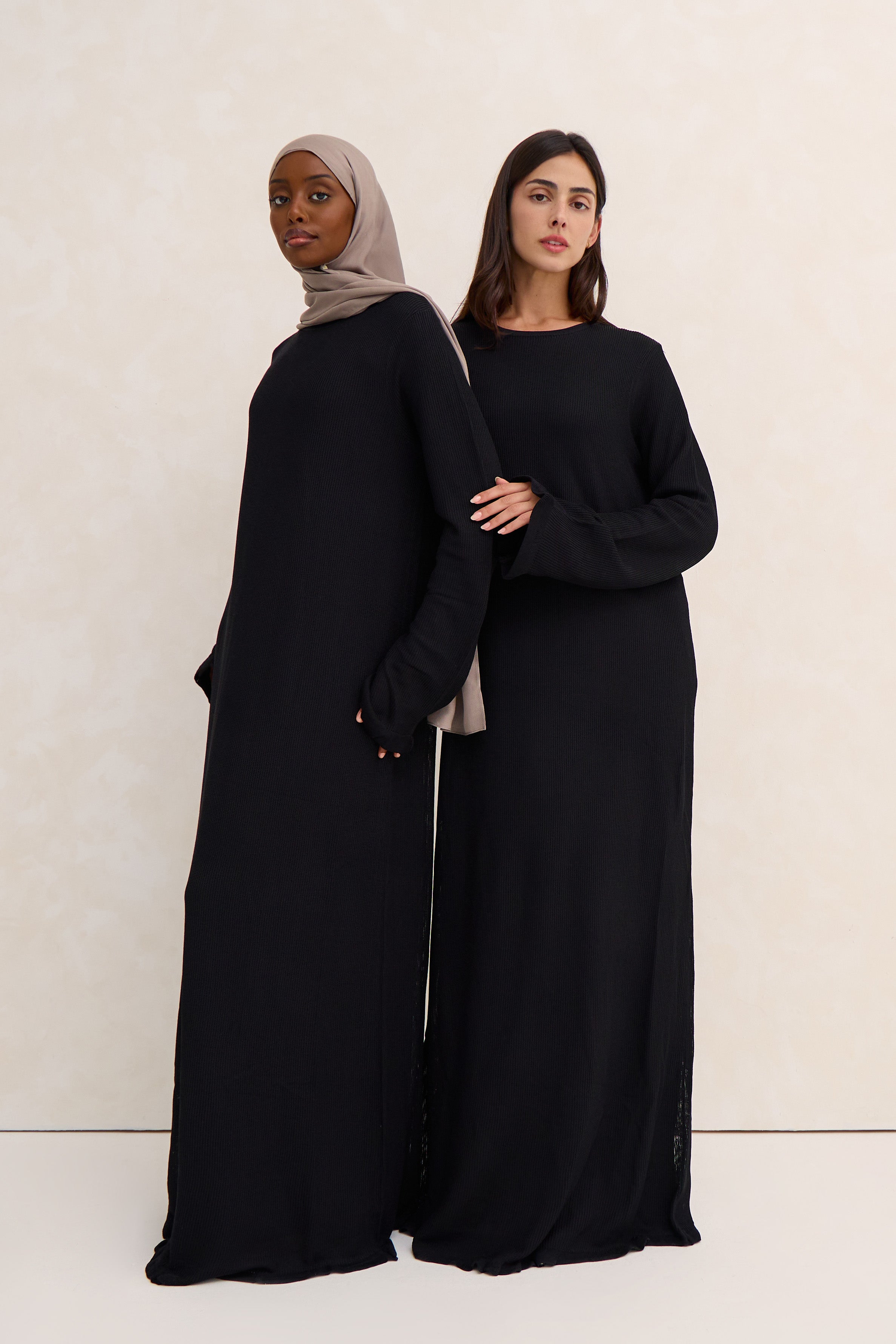 Two women wearing crochet black abayas against a white background
