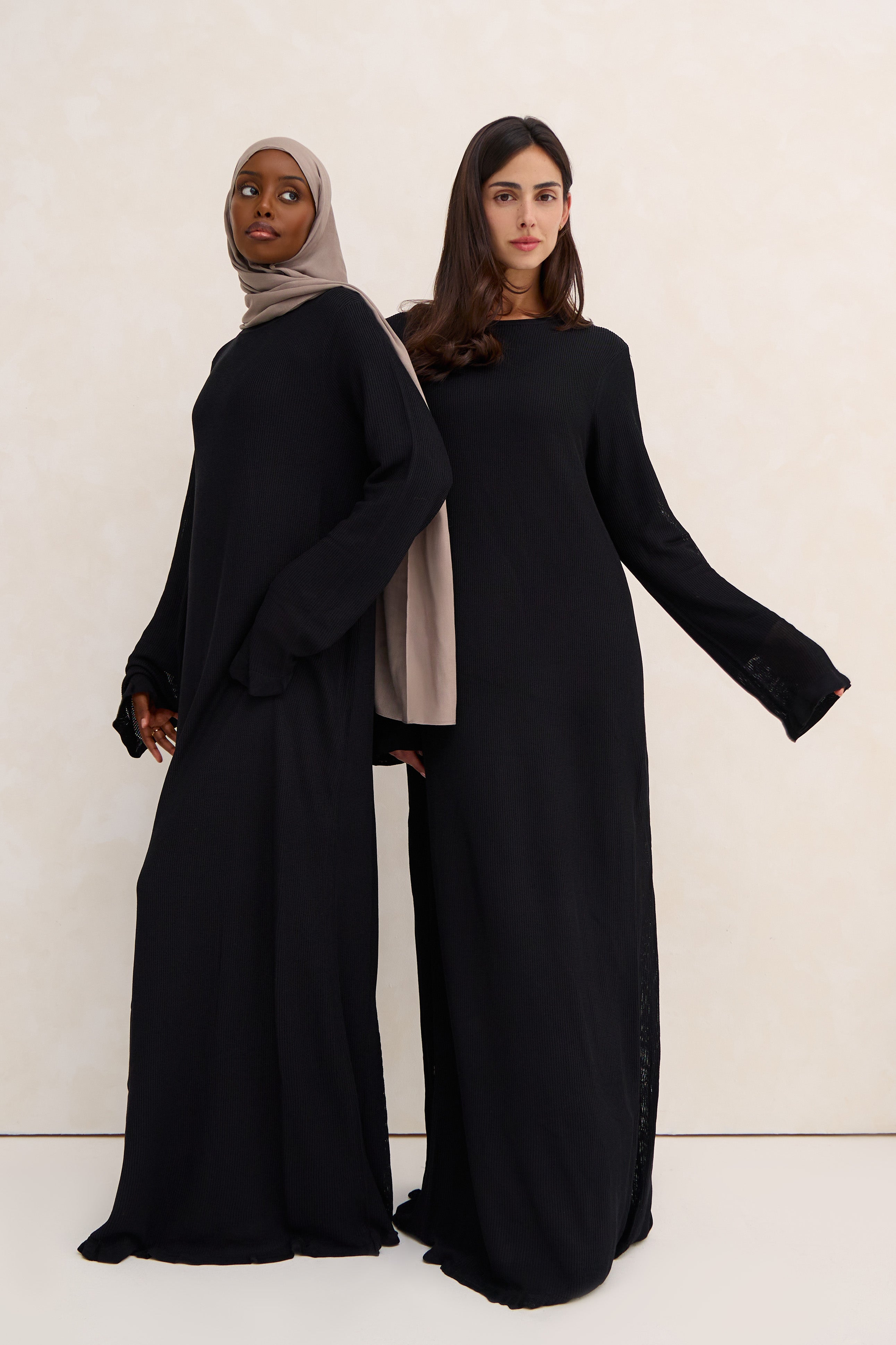 Two women wearing black crochet abayas against a white background