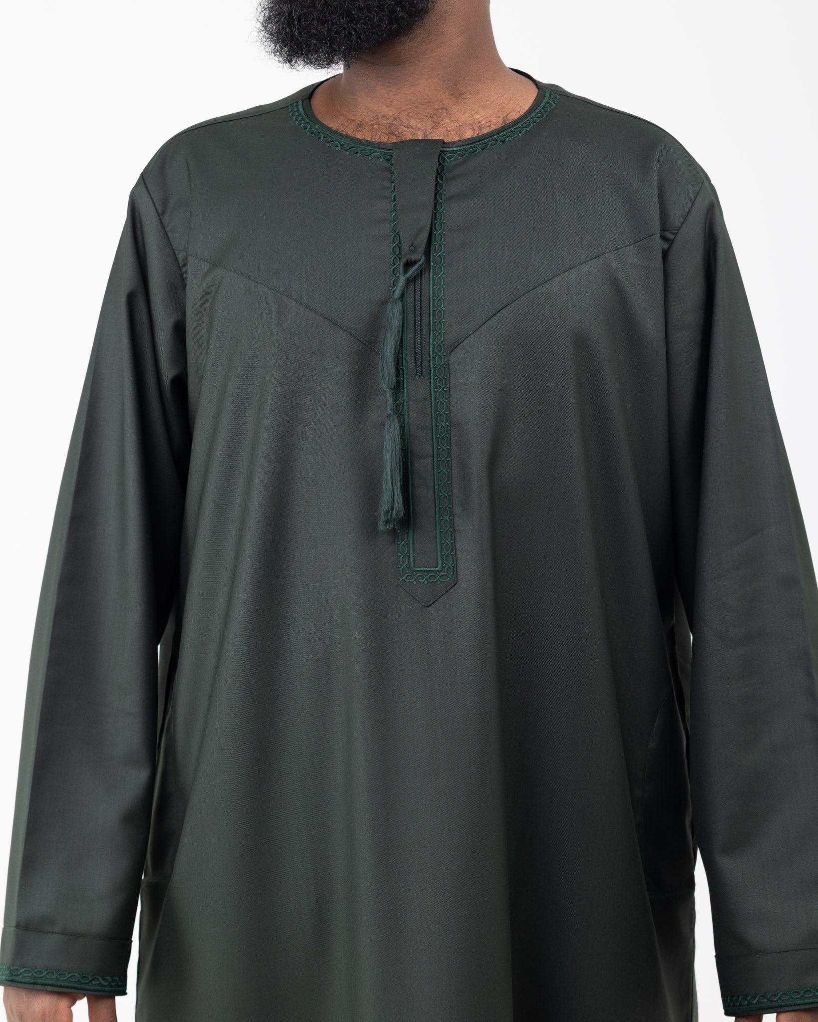 Close up of man standing against a white background wearing an embroidered Rayan green thobe with embroidery on the neckline and cuffs.