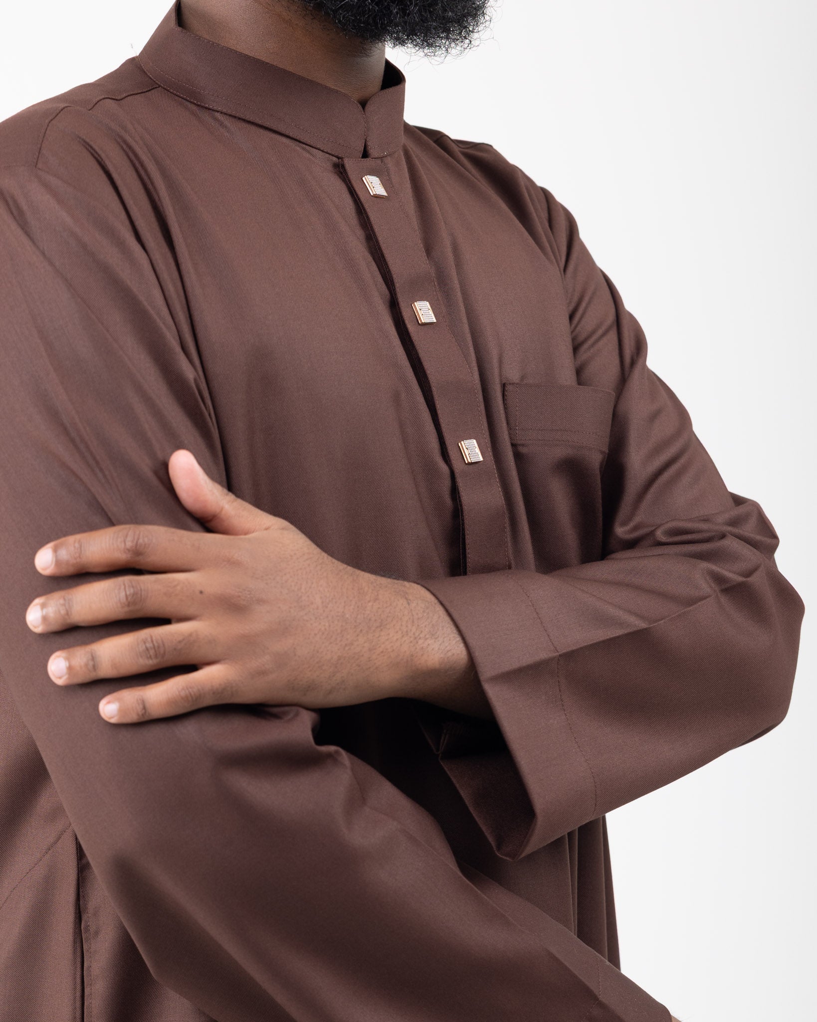 Close up of a man wearing a brown long sleeved collared thobe with a pocket on the chest.
