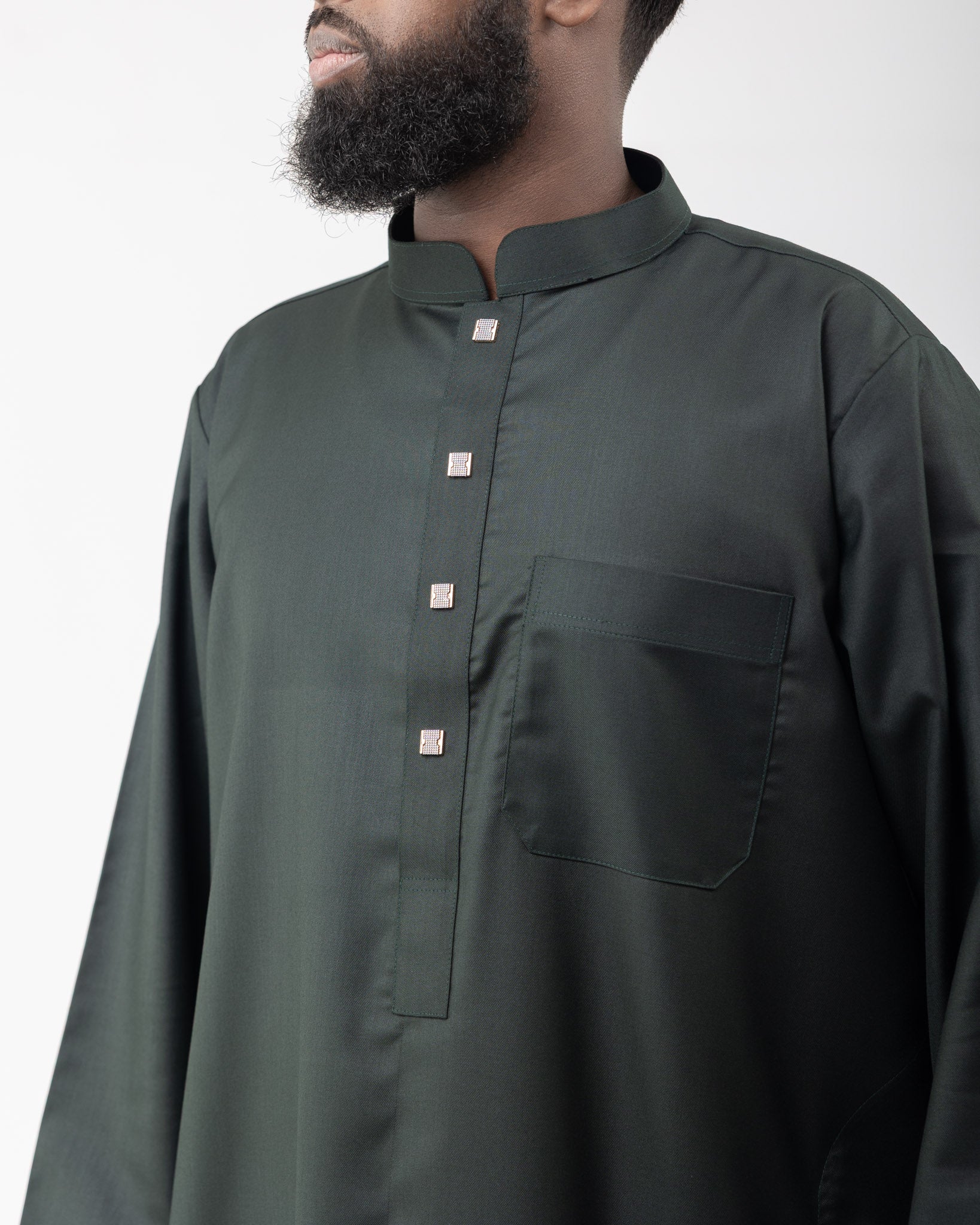 Close up of a man wearing a green long collared thobe with buttoned sleeves.