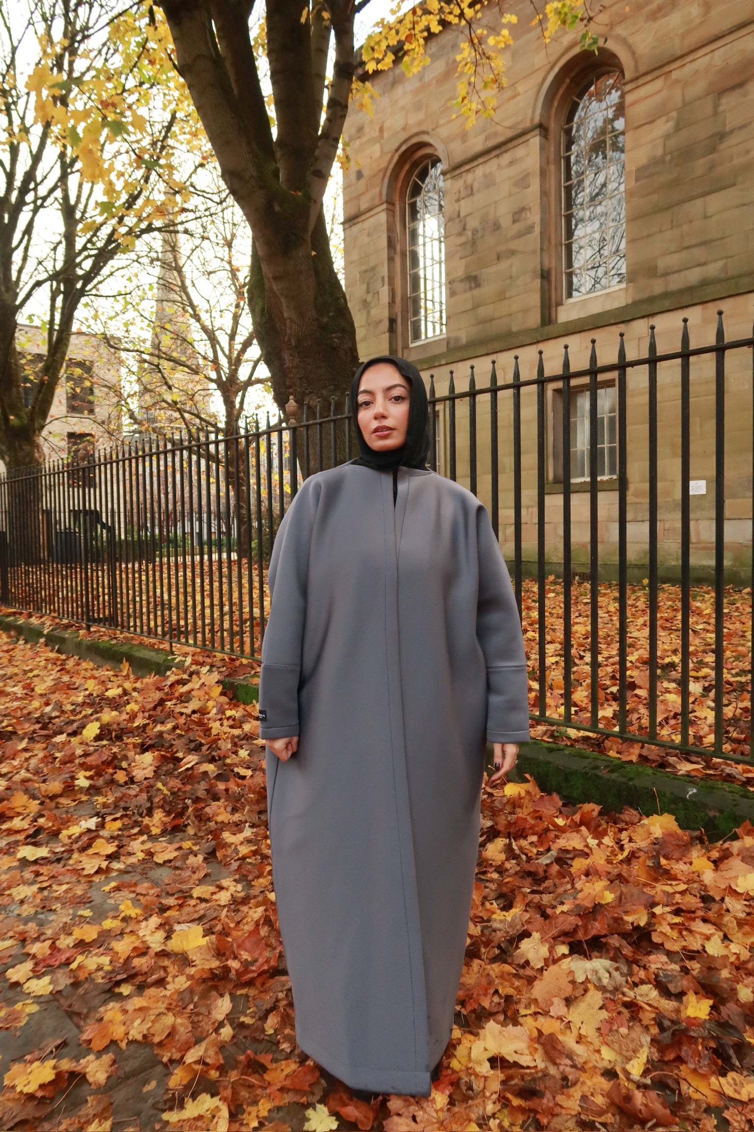 one model wearing neoprene scuba abayas in gray and maroon colors, standing outdoors with autumn leaves on the ground.