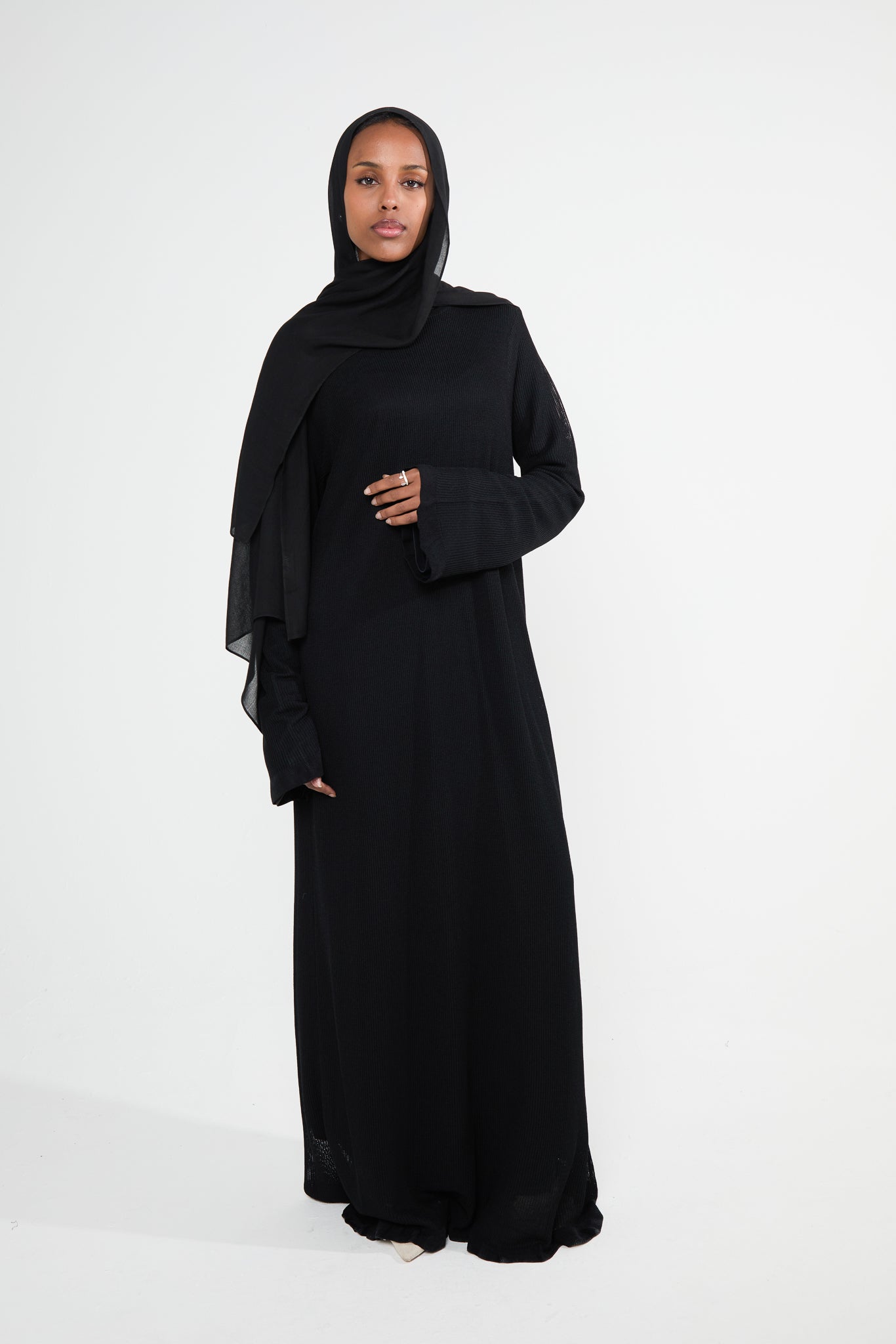 A woman wearing a black lined crochet abaya dress with flared sleeves and a scalloped hem.