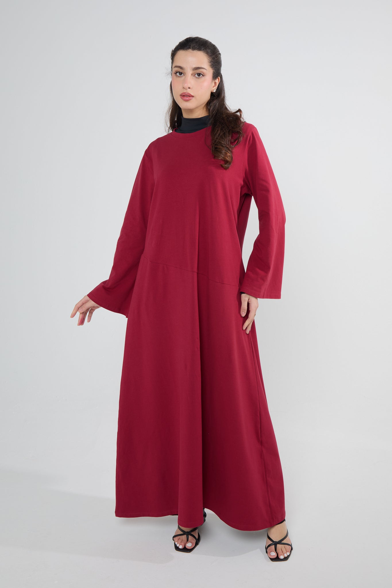 A woman wearing a red Mulberry Cotton Abaya Dress, posing against a white background.