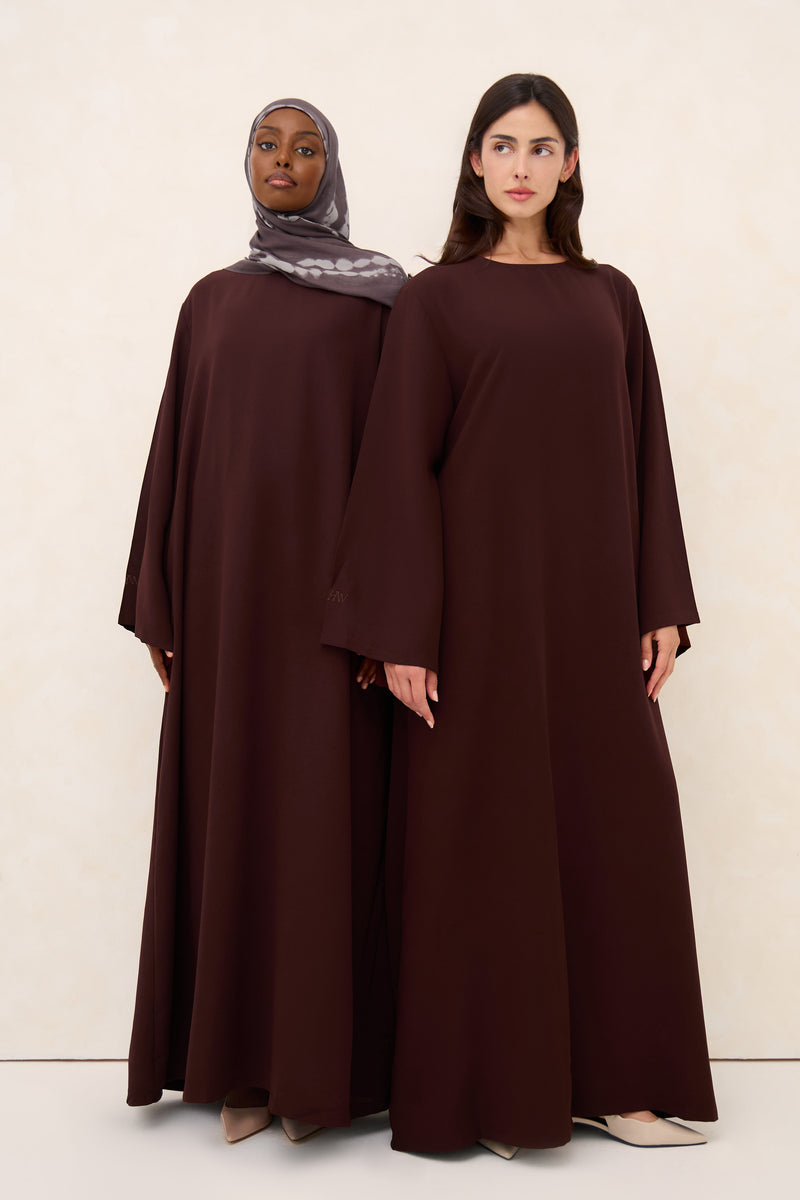 Two women wearing brown cotton abayas against a white background